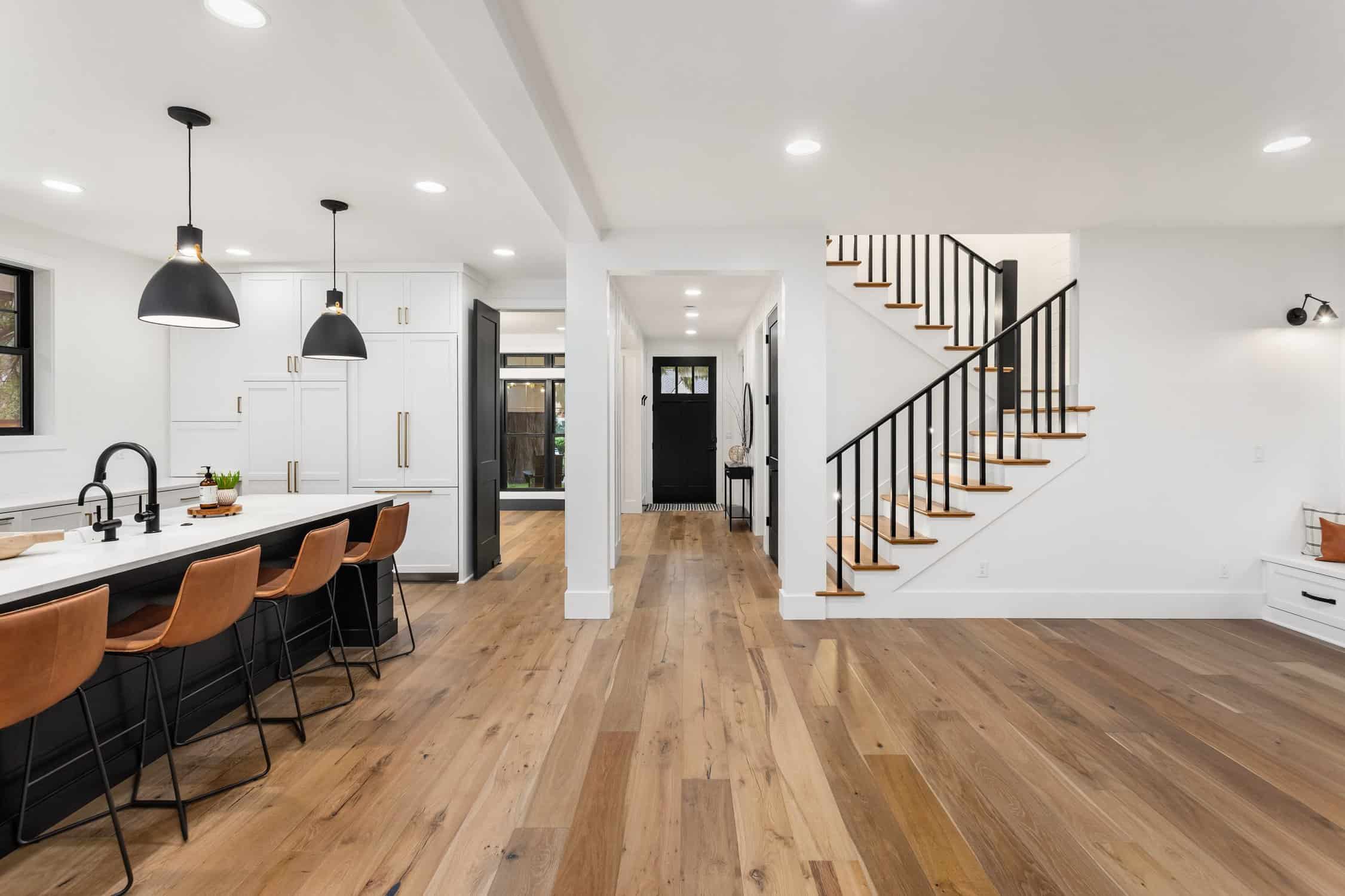 Kitchen and living room interior in new farmhouse style luxury home with open concept floor plan. Features large island with farmhouse sink, hardwood floors, and black accents. interior house painting