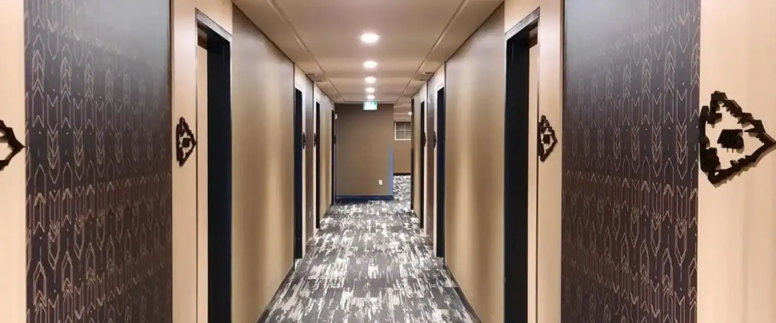 Hotel Corridor Wallpaper Installation and Painting A long hotel corridor featuring patterned wallpaper on the walls and light colored doors.
