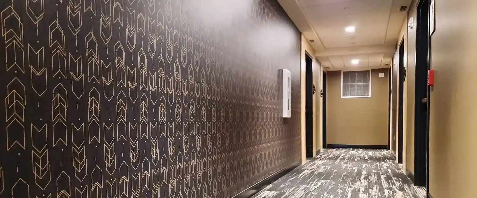 Commercial Hotel Hallway Wallpaper Installation A long hotel hallway with dark patterned wallpaper and light colored walls in the distance.