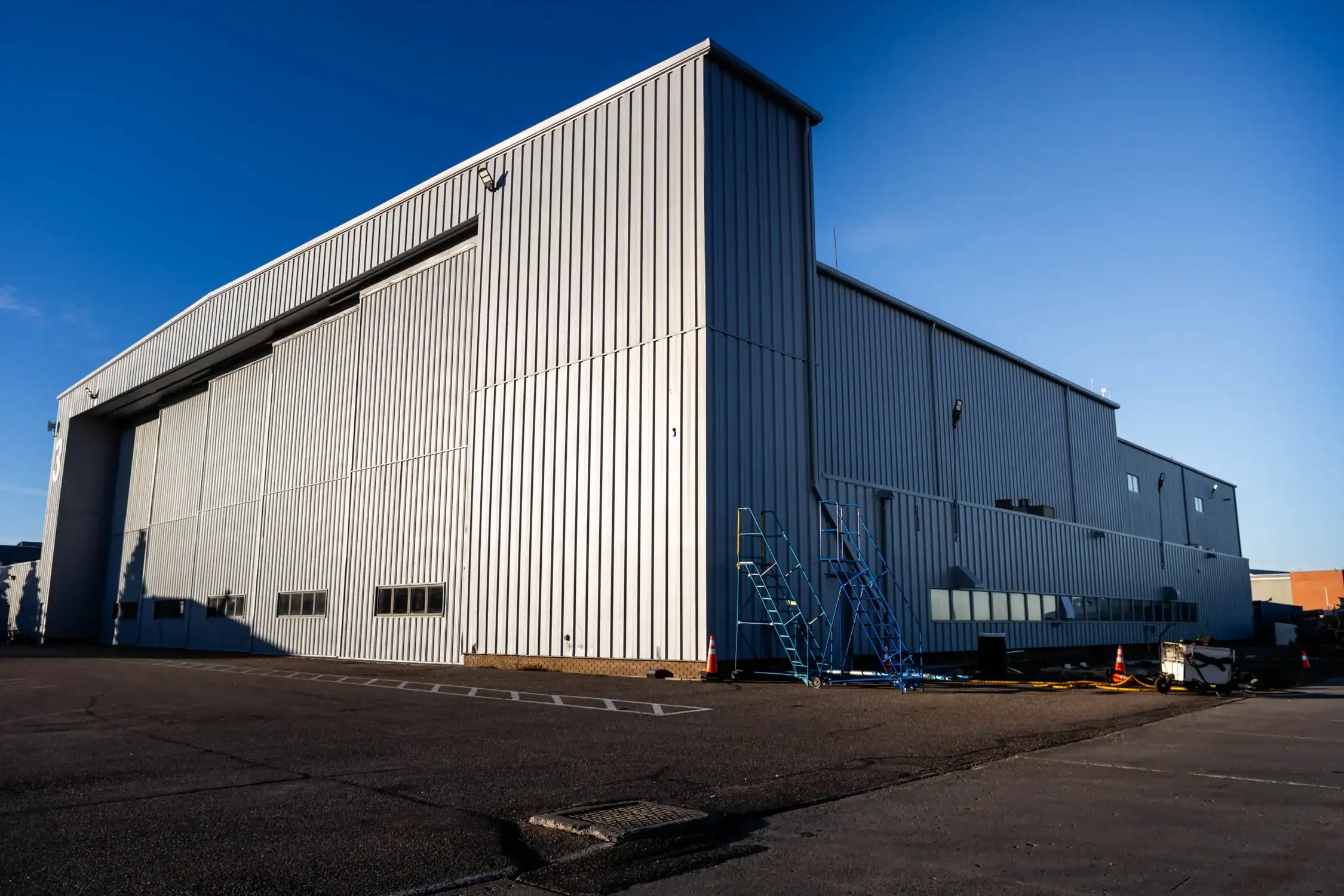 Warehouse and Industrial Building Painting A vast grey industrial warehouse building with corrugated metal siding under a clear blue sky.