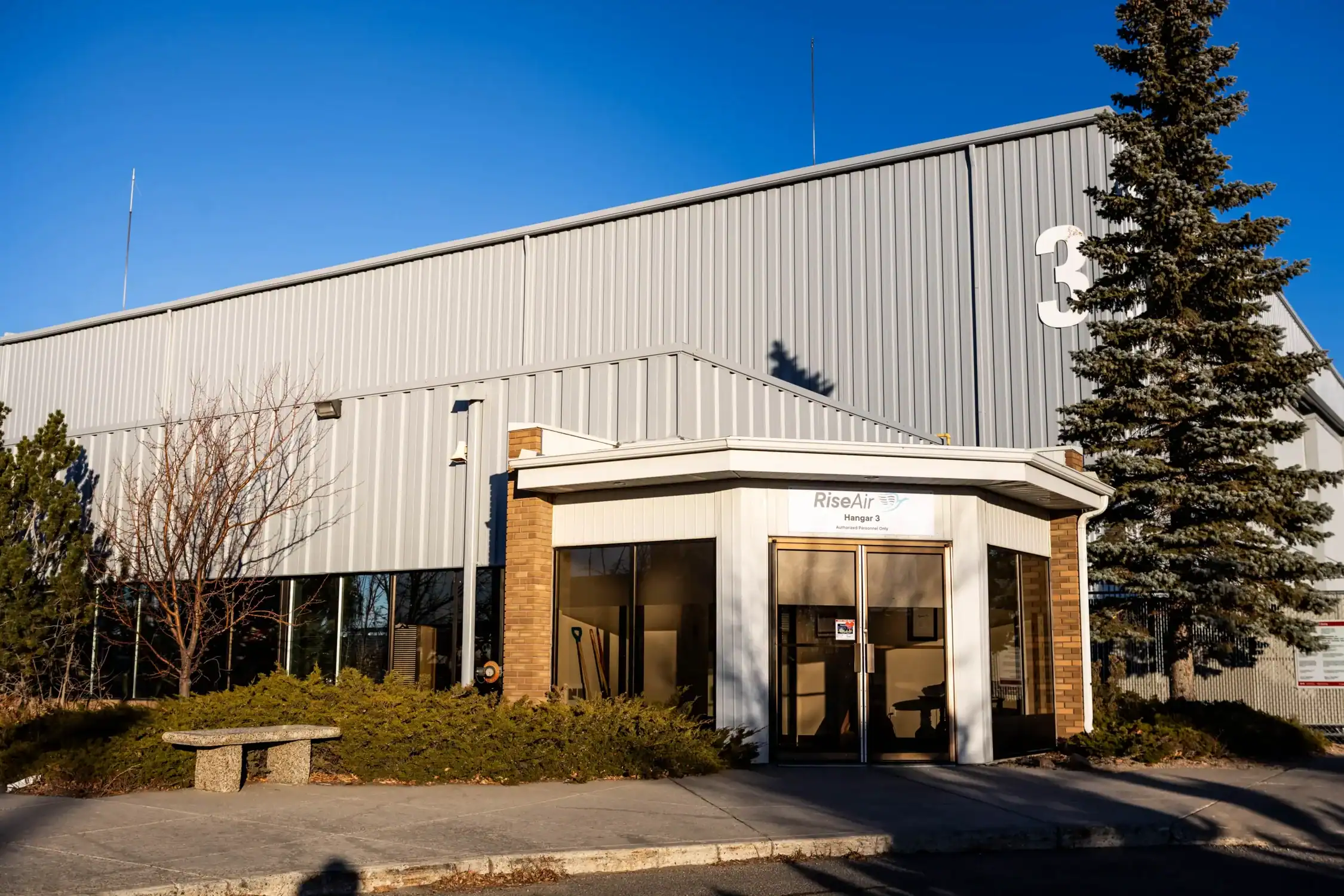 Industrial Building Exterior Painting Services A large grey industrial building with a smaller office entrance and surrounding landscape.
