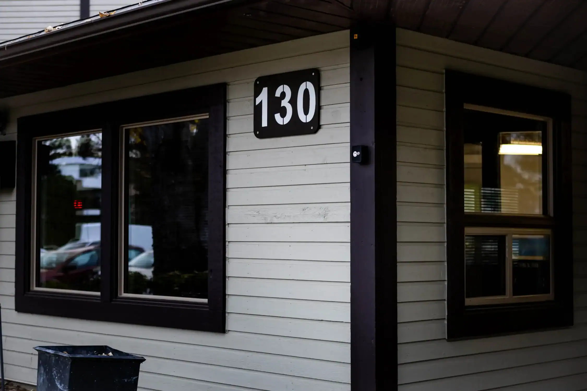 Expert Exterior Painting for Siding and Window Trim Exterior corner of a building with light siding and dark painted window trim, featuring house number 130.