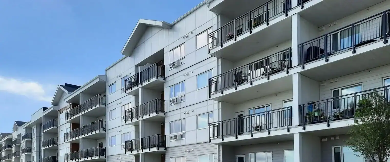 Multi Family and Apartment Building Exterior Painting Services Modern multi story apartment building with light colored exterior and dark balconies under a blue sky.