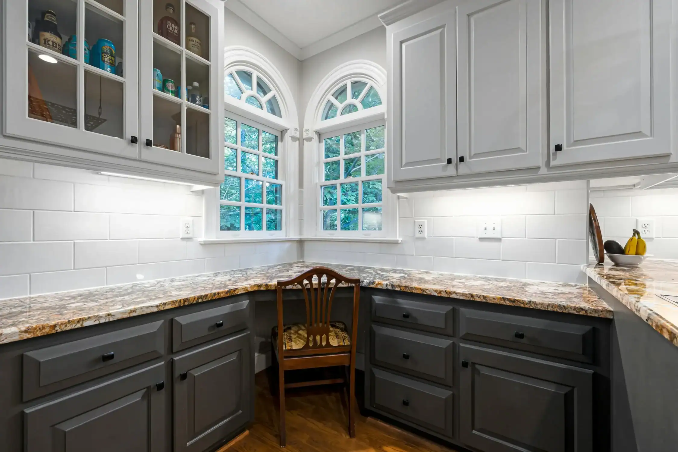 Residential kitchen corner with two toned cabinets, granite countertops, and a built in desk, showcasing quality cabinet painting.
