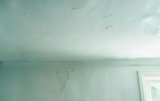 A damaged interior ceiling and wall showing peeling paint, cracks, and visible water stains.