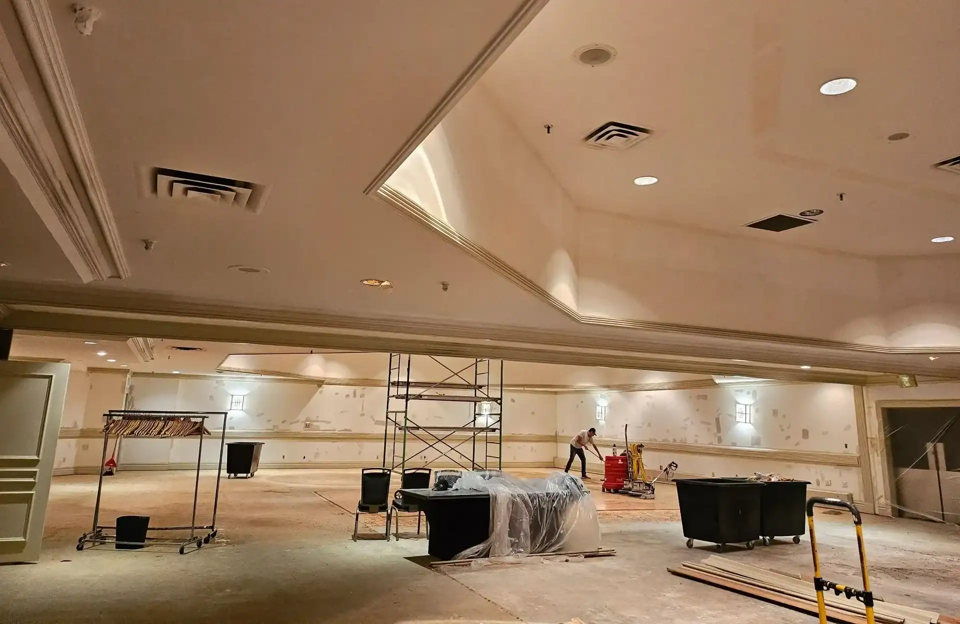 Commercial Renovation Painting in Progress A large commercial room undergoing renovation, with scaffolding and a worker preparing for painting.