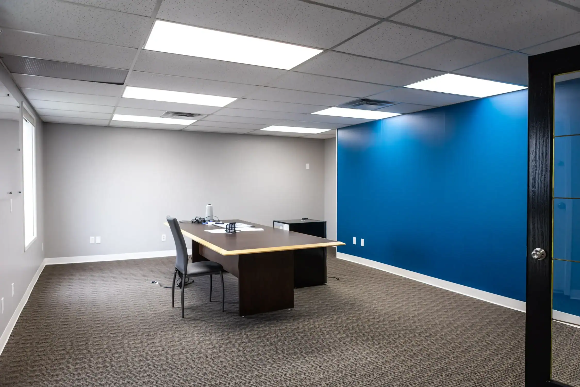 Professional Office Space Interior Painting A professional office space with a blue accent wall, grey walls, and a large conference table.