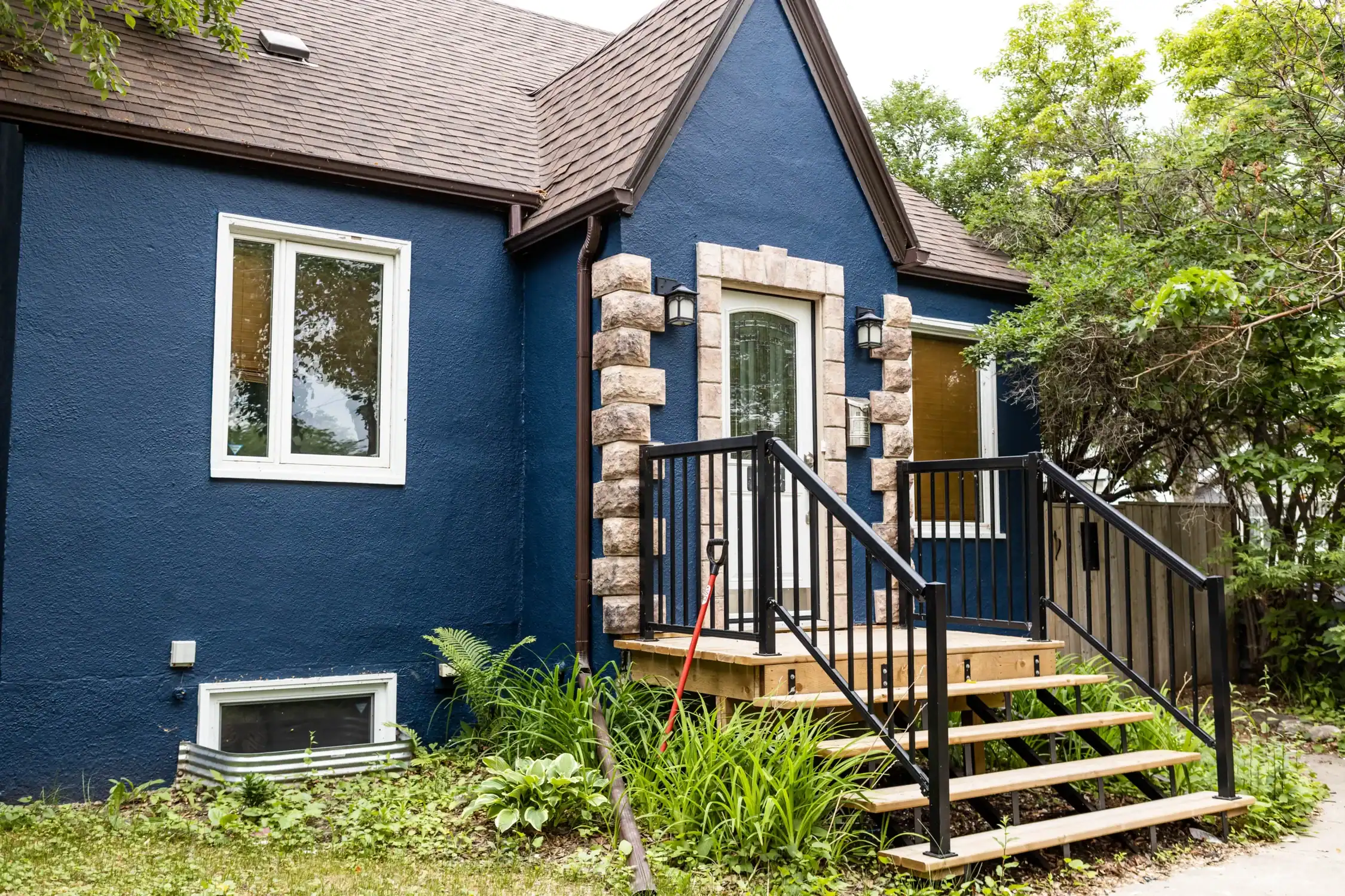 Residential Stucco Exterior Painting and Home Facade Renovation A residential house with a dark blue stucco exterior, stone accents, and a newly painted front porch.