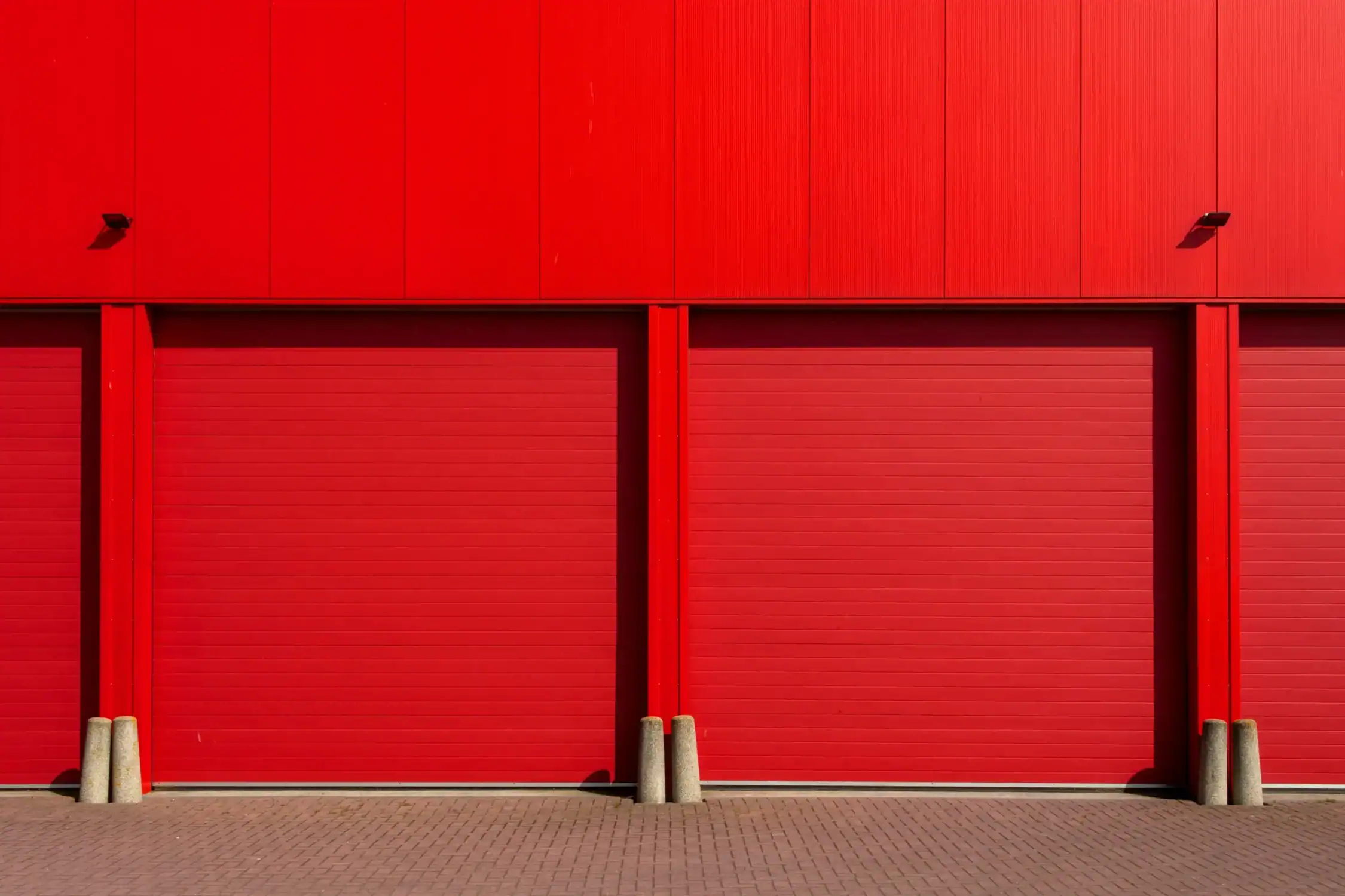 Industrial Building Exterior Painting Service A vibrant red industrial building exterior featuring multiple large roll up garage doors.