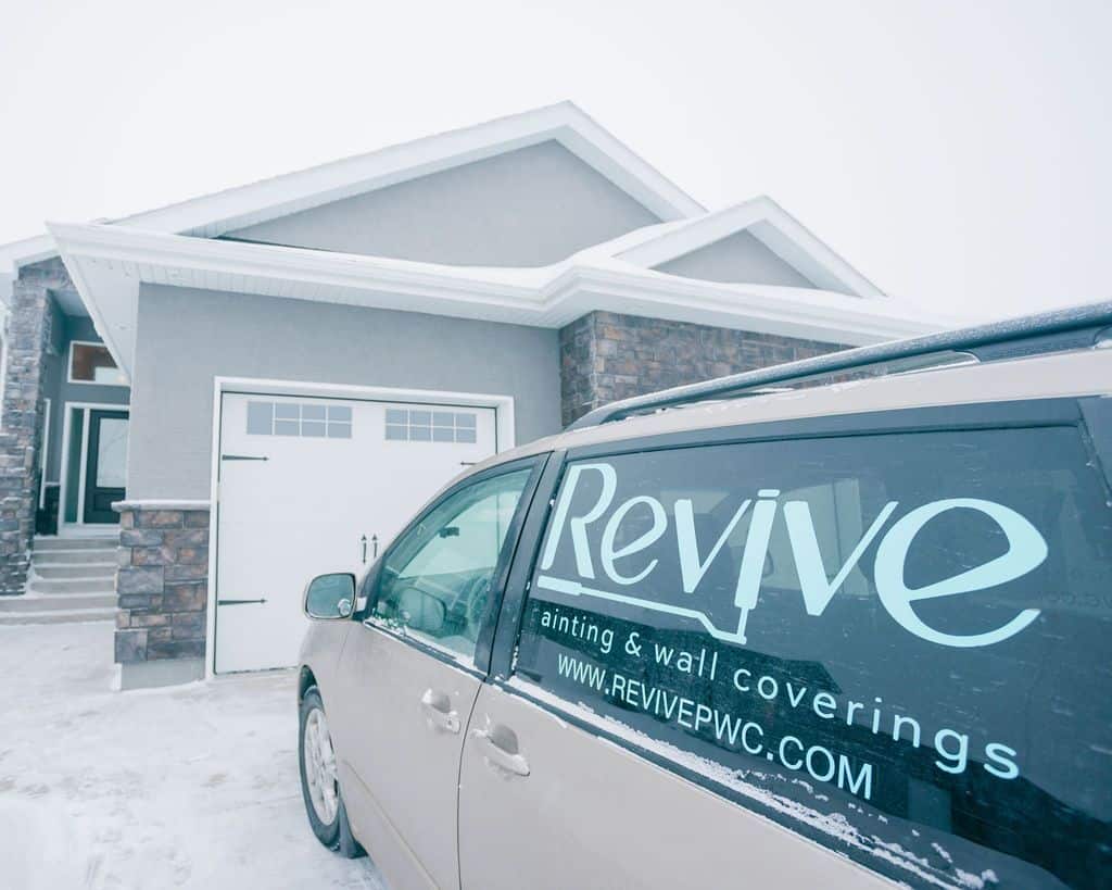 A Revive painting company van parked in front of a newly painted house in a snowy winter setting.