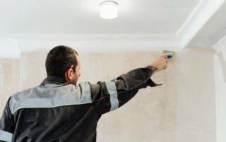 A professional painter meticulously applies paint to the crown molding and ceiling edge in a room.