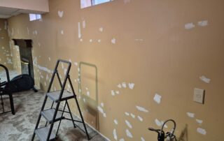 An interior room with beige walls showing numerous white patches, indicating extensive wall repair before painting.