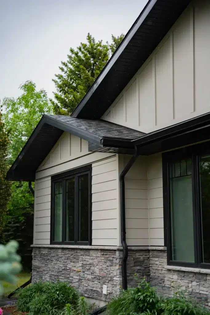 Side View of Modern House Exterior with Light Siding and Dark Windows Side view of a modern house exterior showcasing light beige siding, dark windows, and a stone foundation.