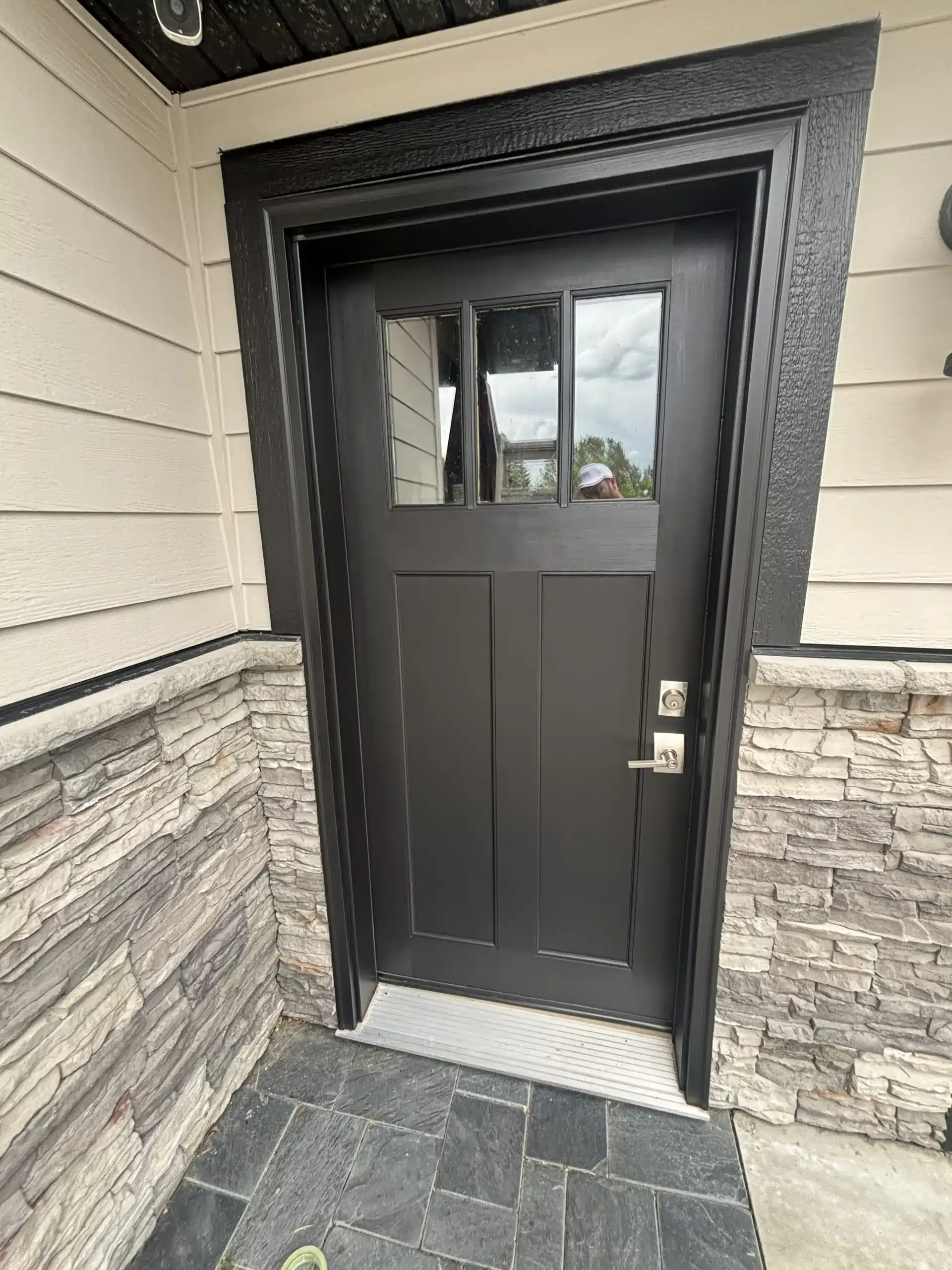 Freshly Painted Black Exterior Front Door and Trim A newly painted black exterior front door with matching trim on a house with light siding and stone veneer.
