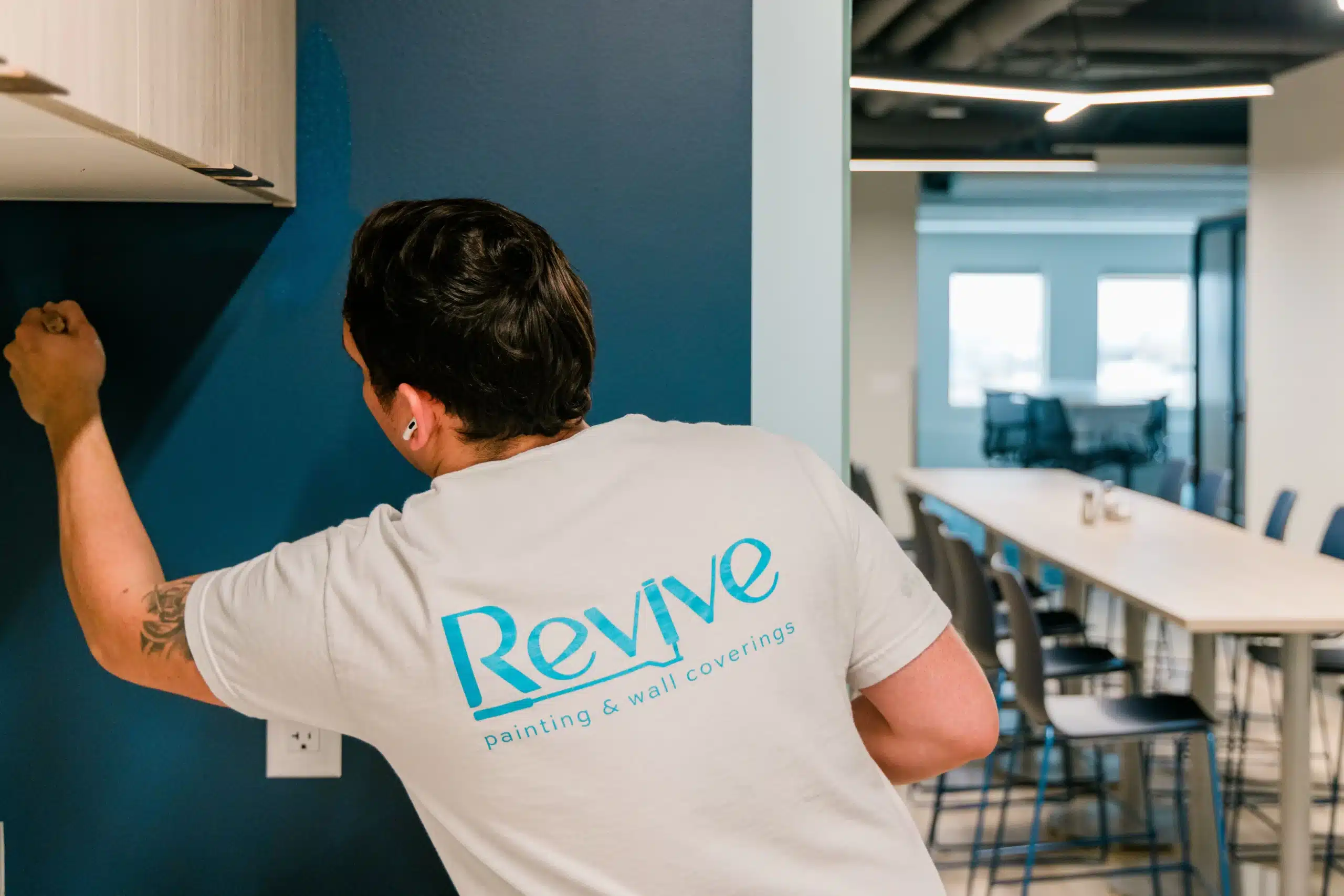 Commercial Interior Painting and Wall Covering Services Professional painter working on a dark blue wall in a modern commercial office space.